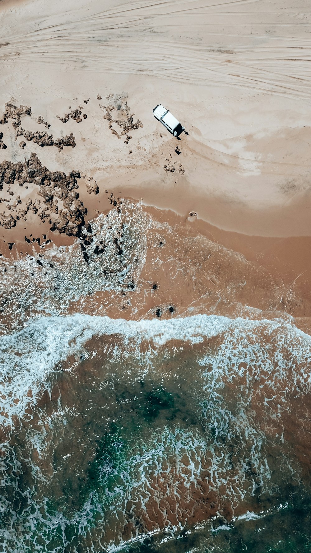 an aerial view of a beach with a vehicle in the water