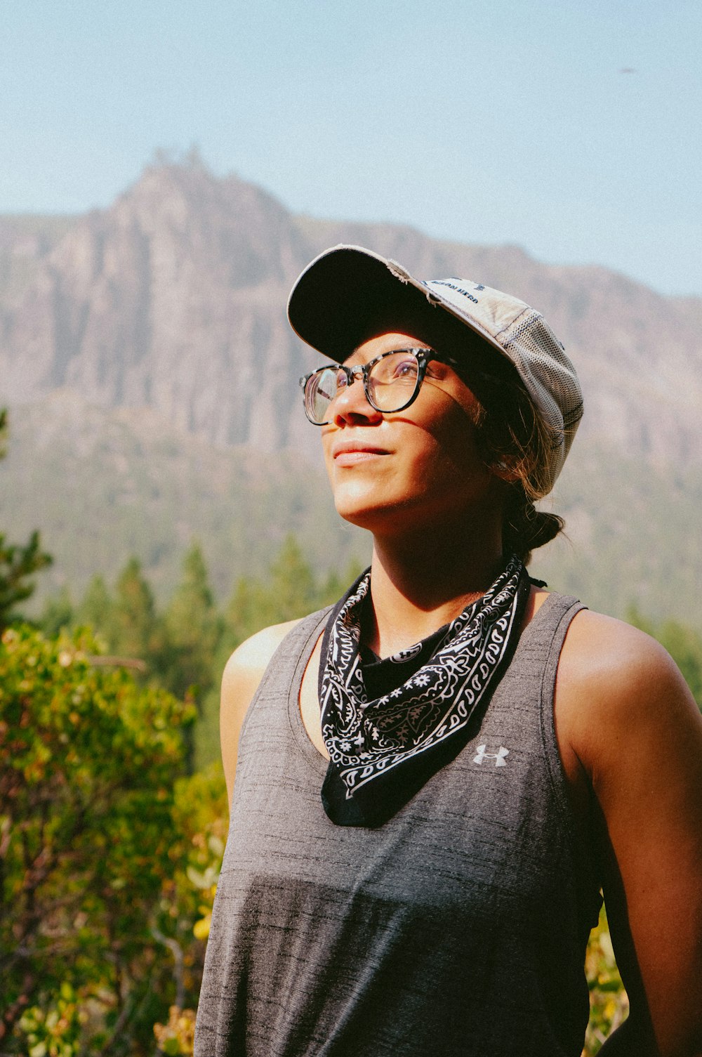 a woman wearing a hat and glasses standing in front of a mountain