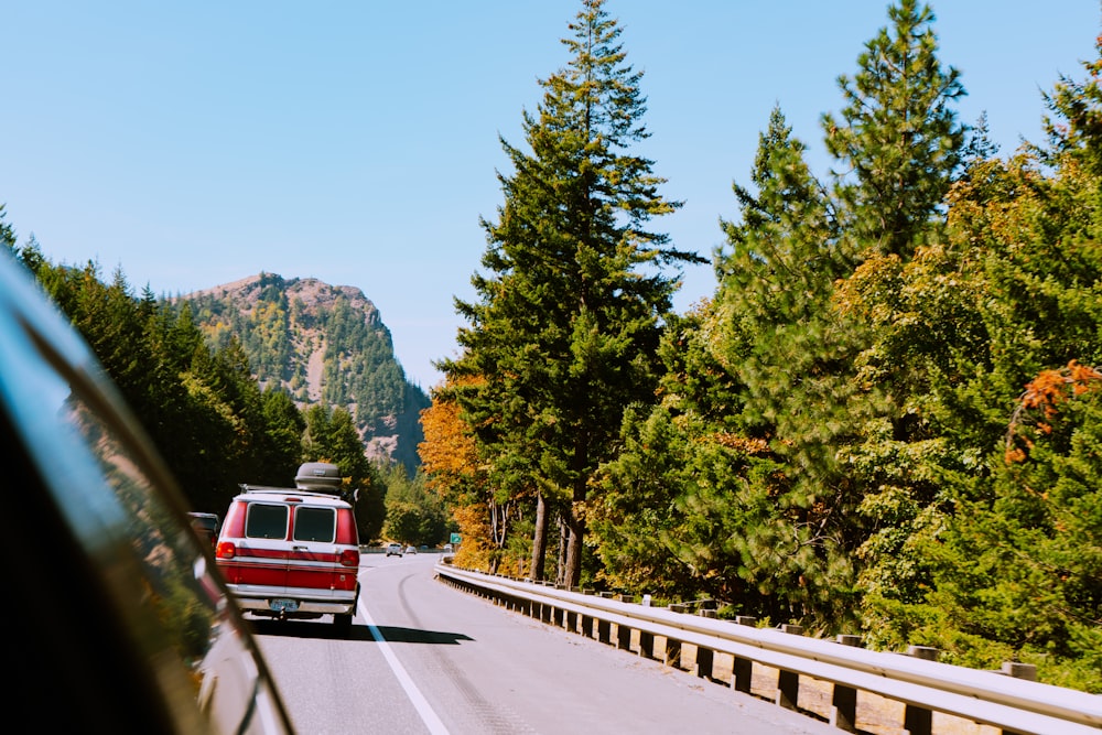 a red van driving down a road next to a forest