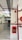 A corridor with tiled floor and walls partially lined with wood. Red fire safety equipment, including pipes and a fire hose cabinet, is mounted on the walls. Above, there are industrial ceiling fixtures and a green emergency exit sign.