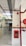 A corridor with tiled floor and walls partially lined with wood. Red fire safety equipment, including pipes and a fire hose cabinet, is mounted on the walls. Above, there are industrial ceiling fixtures and a green emergency exit sign.