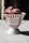 A stylish white bowl with red vertical stripes and text reading 'Pure Fresh Ice Cream' contains a generous serving of pink ice cream. The setup is on a light gray surface with a dark blurred background, suggesting natural light casting shadows.