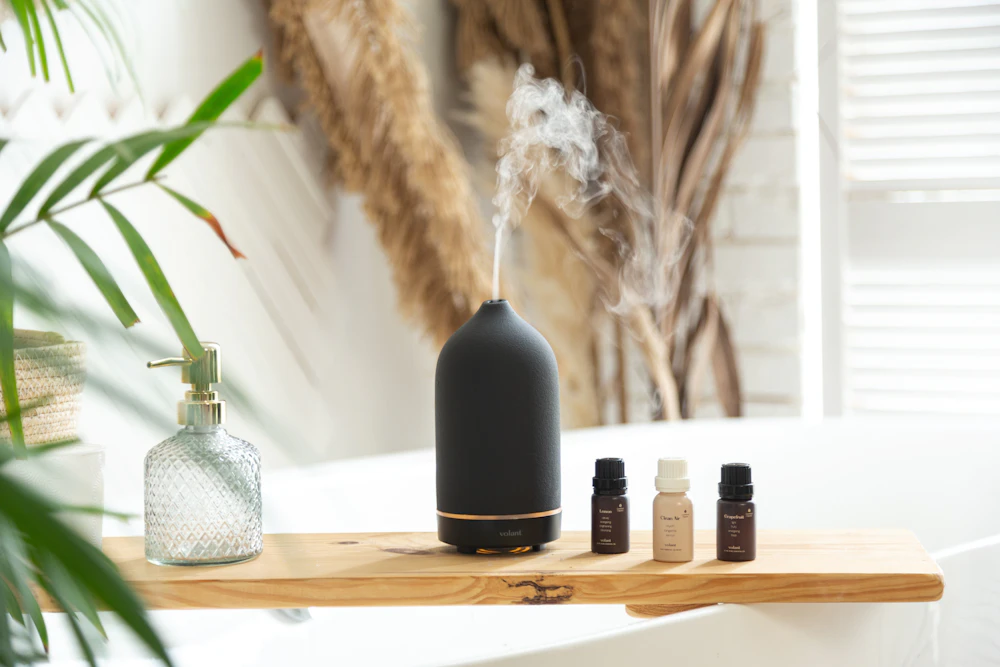 Black ceramic diffuser releasing steam beside oil bottles