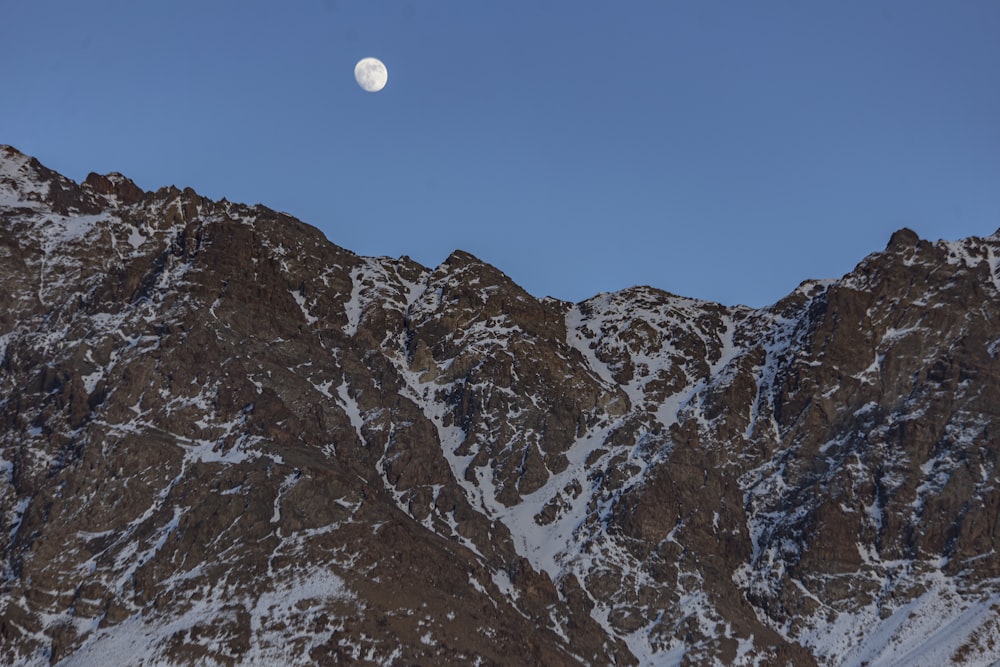 a full moon is seen above a snowy mountain