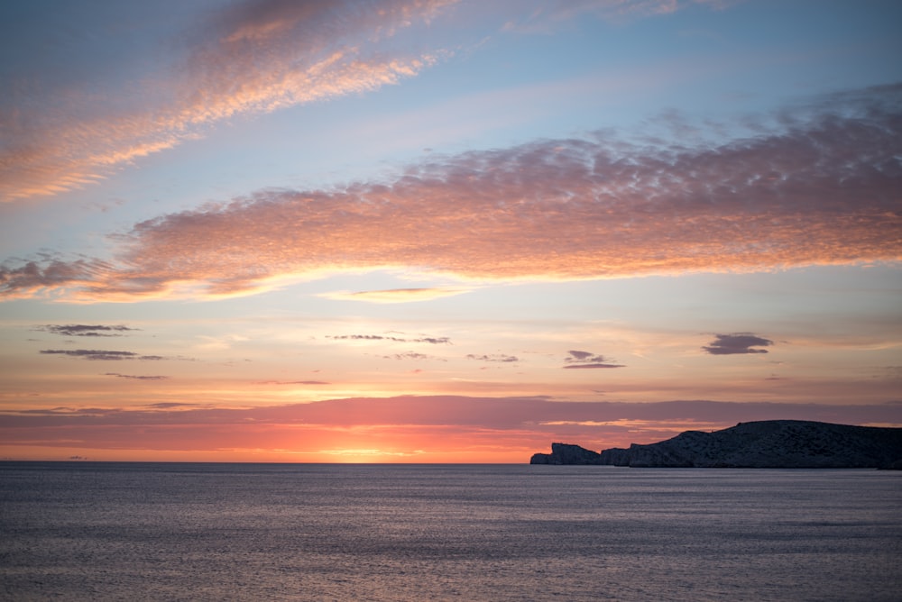 the sun is setting over the ocean with a small island in the distance