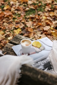 Close-up of a steaming cup of coffee resting on a wooden stump, surrounded by pinecones and autumn leaves.