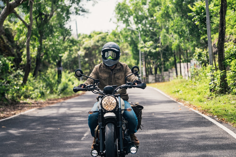 a man riding a motorcycle down a tree lined road