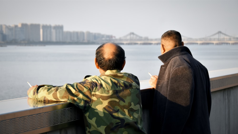 a couple of men standing next to each other near a body of water