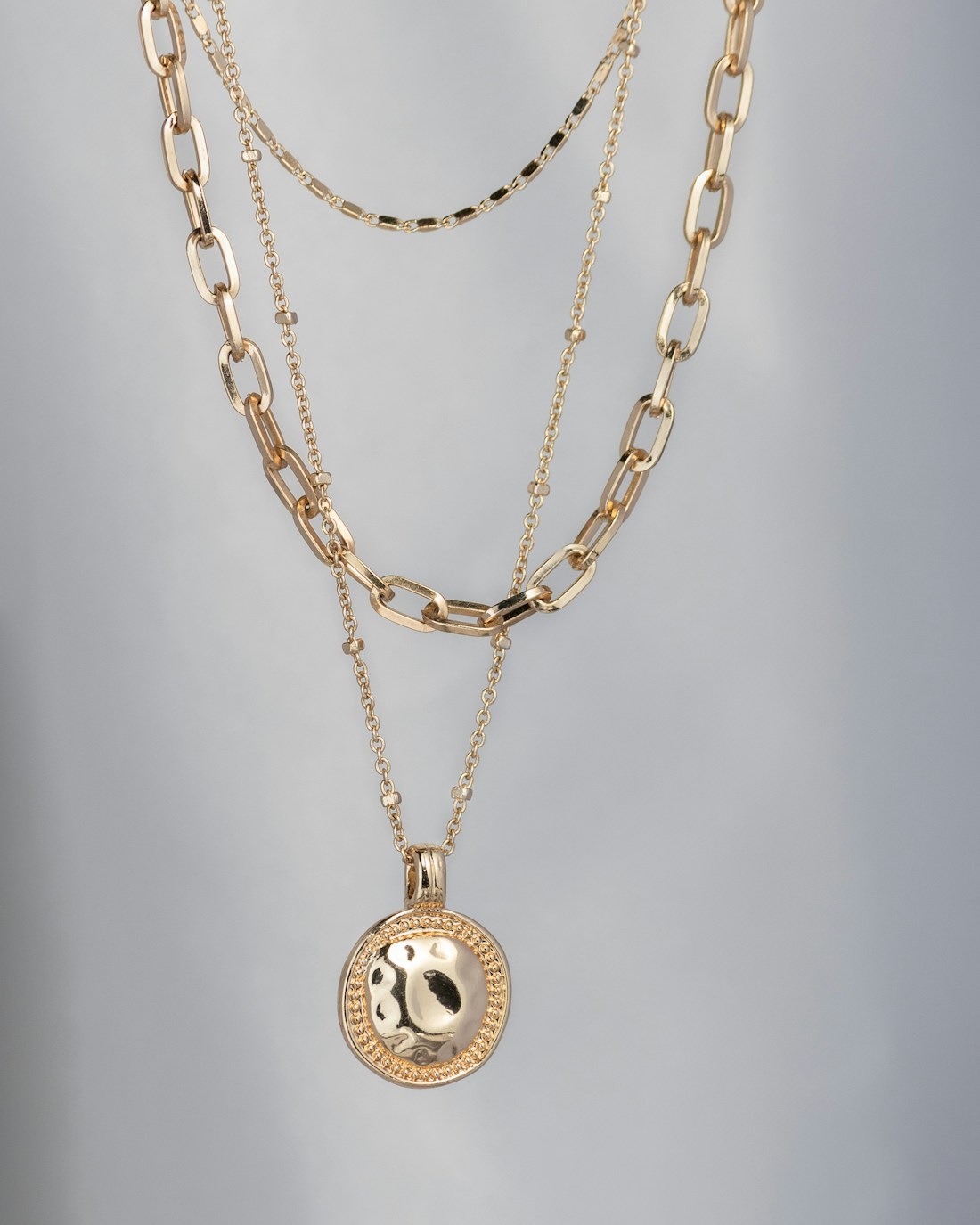Three layered gold chains with a hammered medallion on a pale backdrop
