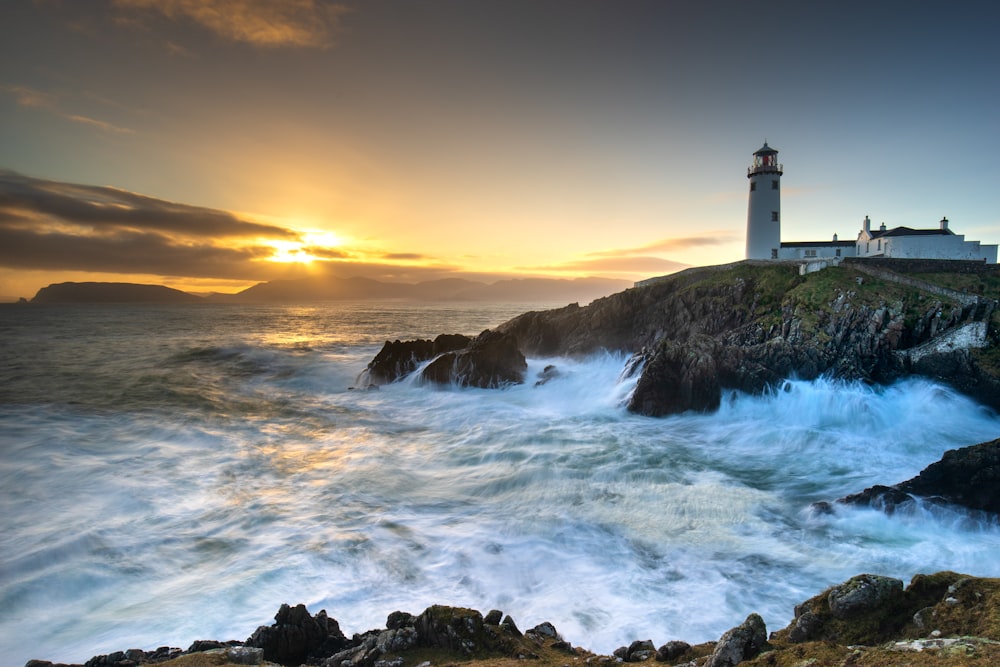 a lighthouse on a rocky shore with waves crashing in front of it