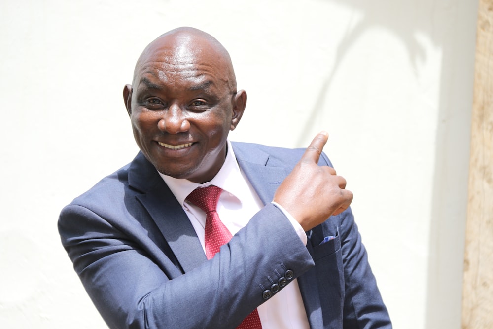 a man in a suit and red tie giving a thumbs up