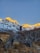 A climber standing triumphantly on a snowy Himalayan peak at sunrise, with crisp blue sky overhead.
