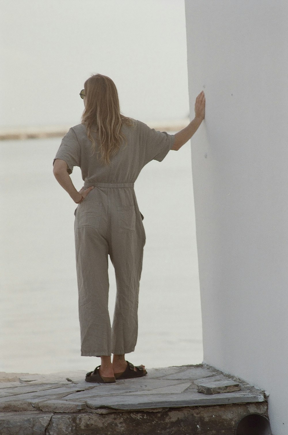 a woman leaning against a wall by the water