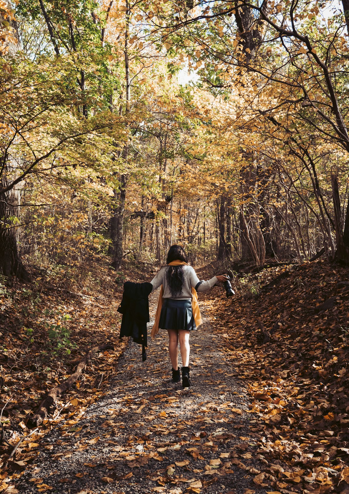 A woman walking alone down a forest path covered in fallen autumn leaves