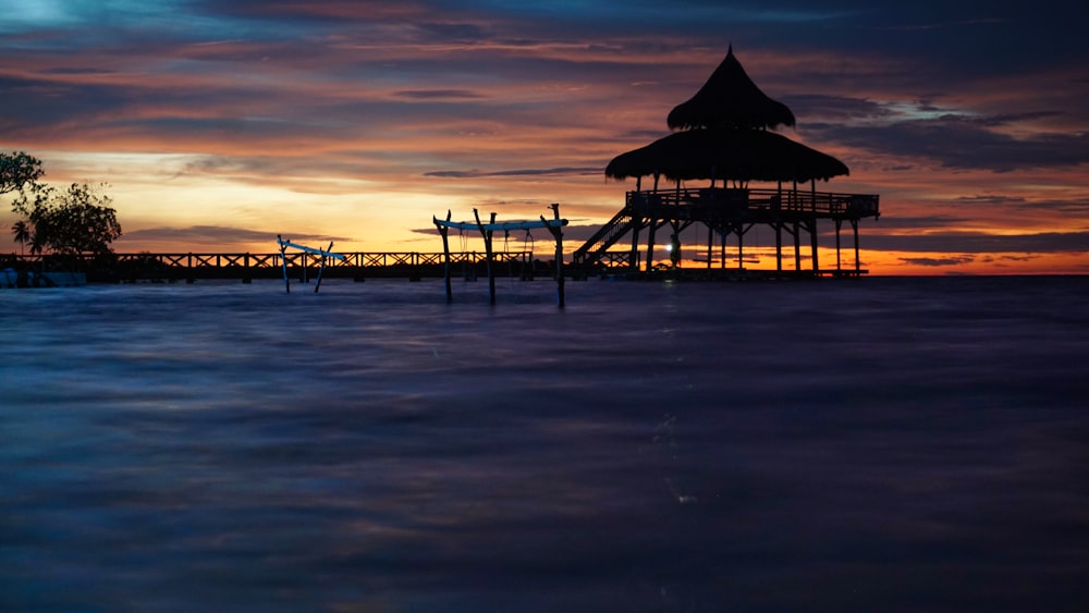 a sunset view of a pier with a gazebo in the distance