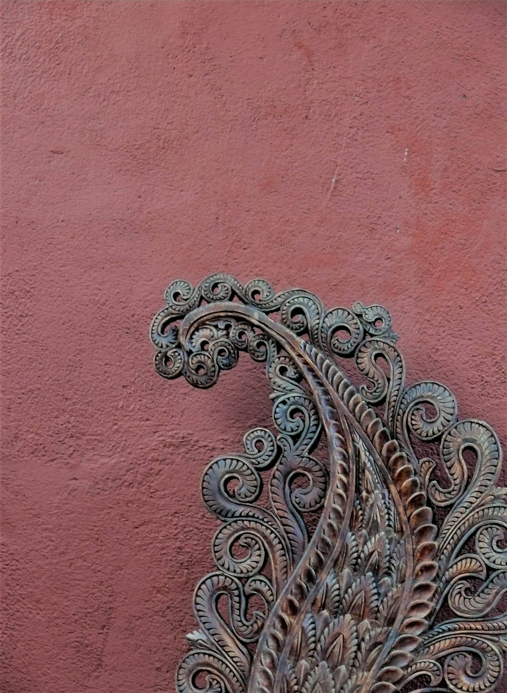 a metal peacock sculpture on a pink wall