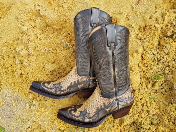 A worn pair of cowboy boots standing on dusty desert ground with cacti in the background.