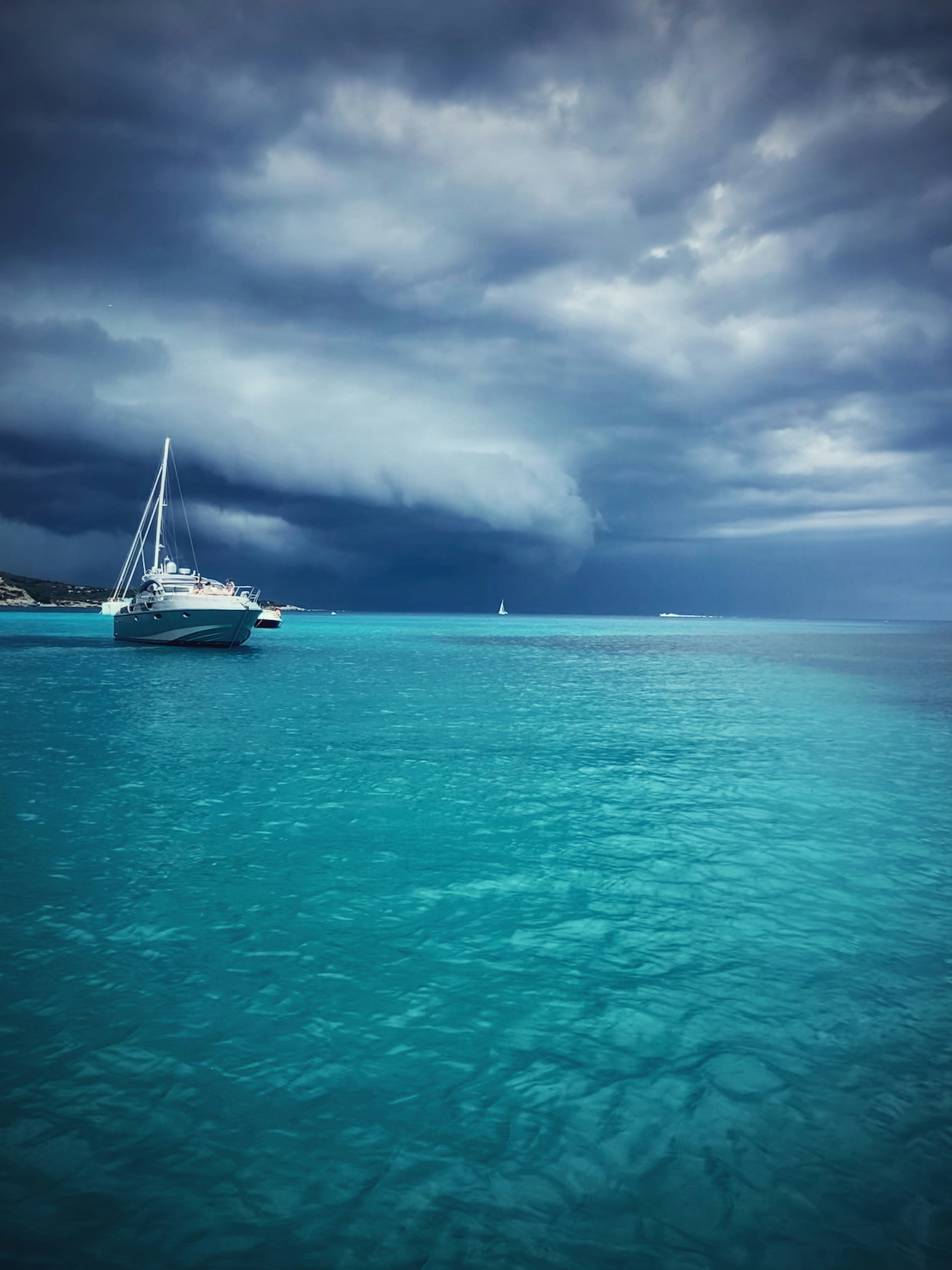 Crystal clear turquoise ocean waters with private yacht, deep shadows under deck, dramatic overcast sky, dark sea below