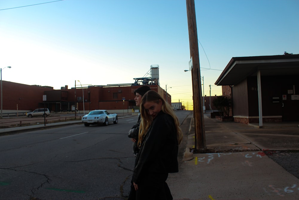 a woman walking down a street next to a white car