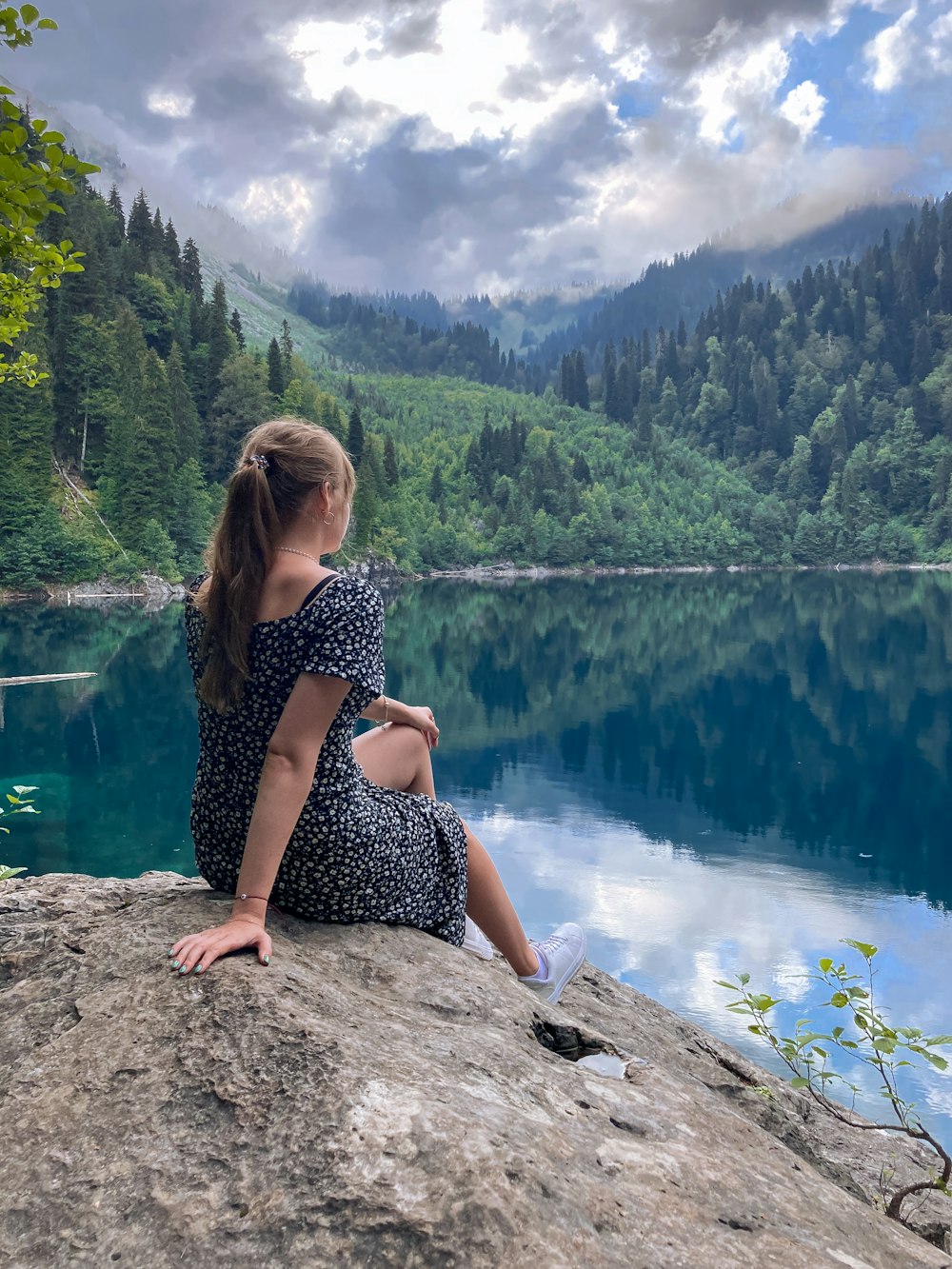 a woman sitting on top of a rock next to a lake