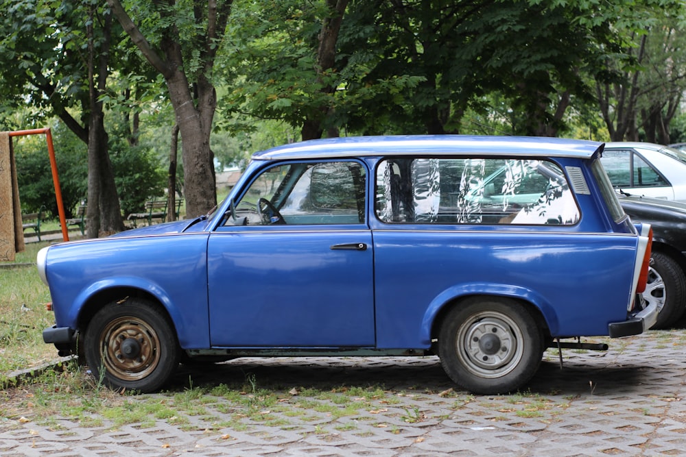 an old blue car parked on a cobblestone road