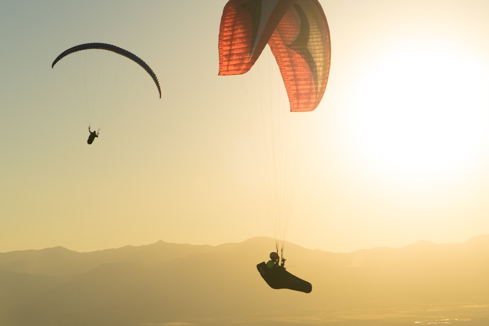 two people parasailing in the sky with mountains in the background