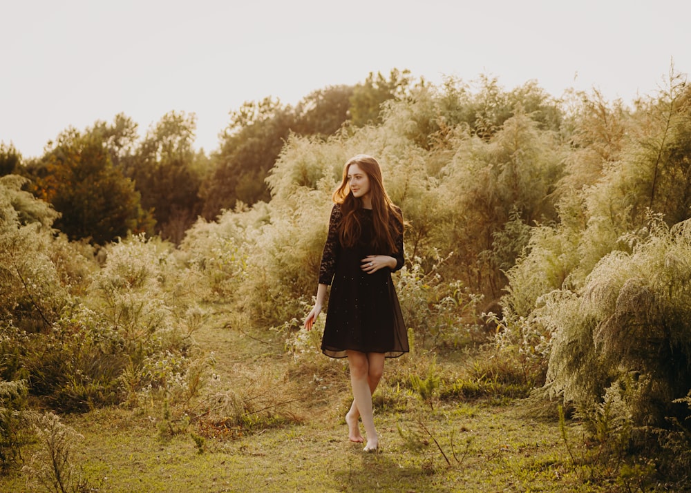 a woman in a black dress walking through a field