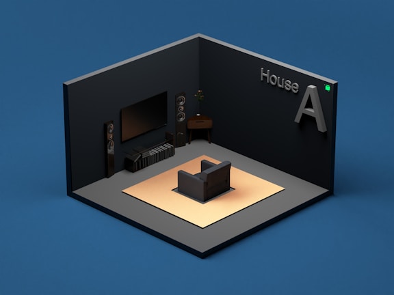 A modern, minimalist living room setup within a small, enclosed space. The room features a large flat-screen television mounted on the wall, flanked by tall speakers on both sides. There is a single, cushioned armchair placed on a light-colored rug. A small side table with a plant on it is placed next to the television. The walls are dark-colored, and the floor is gray. The words 'House A' are displayed prominently in 3D text on one of the walls.