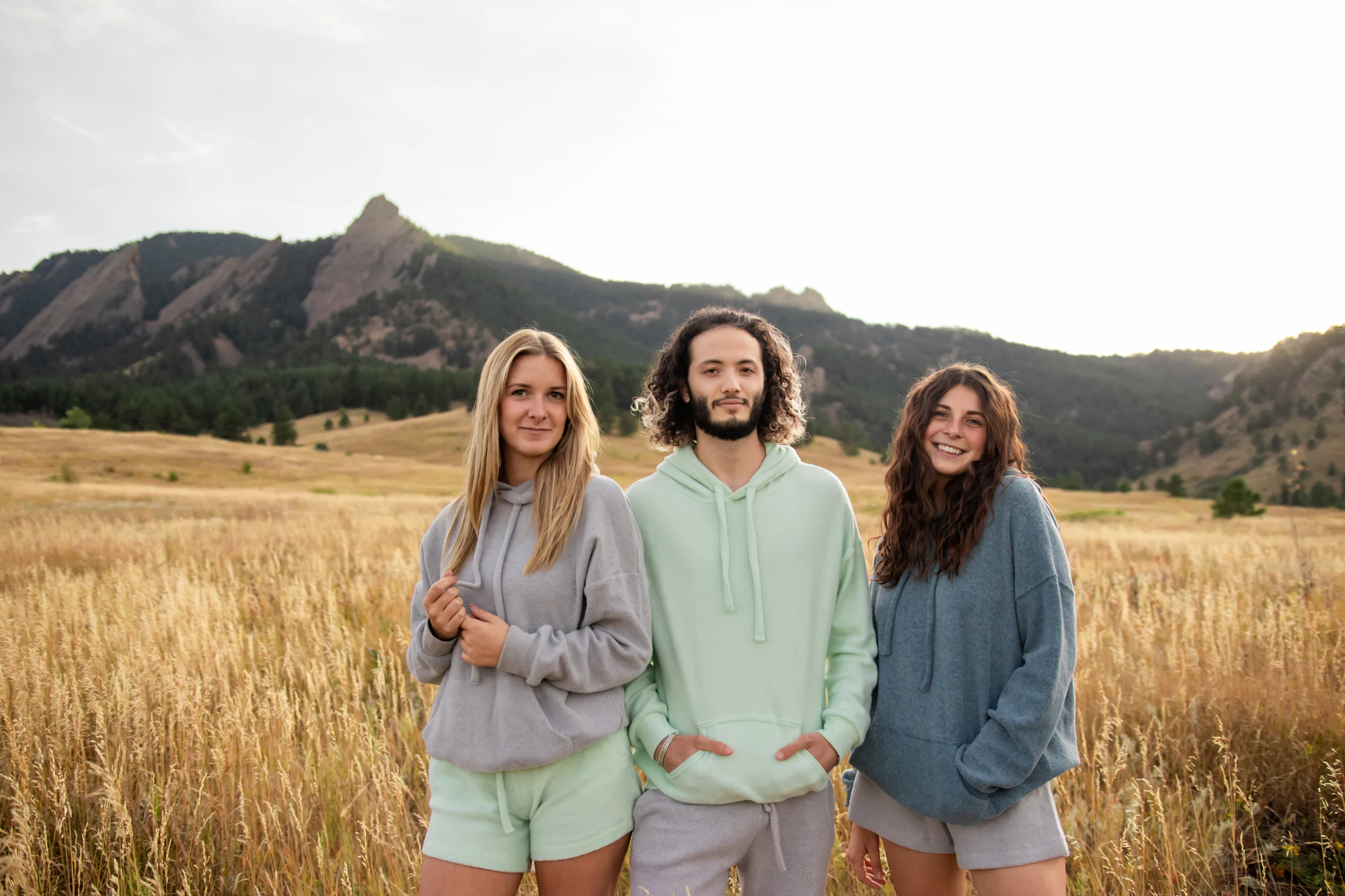Three friends in plain hoodies standing in a field of tall grass