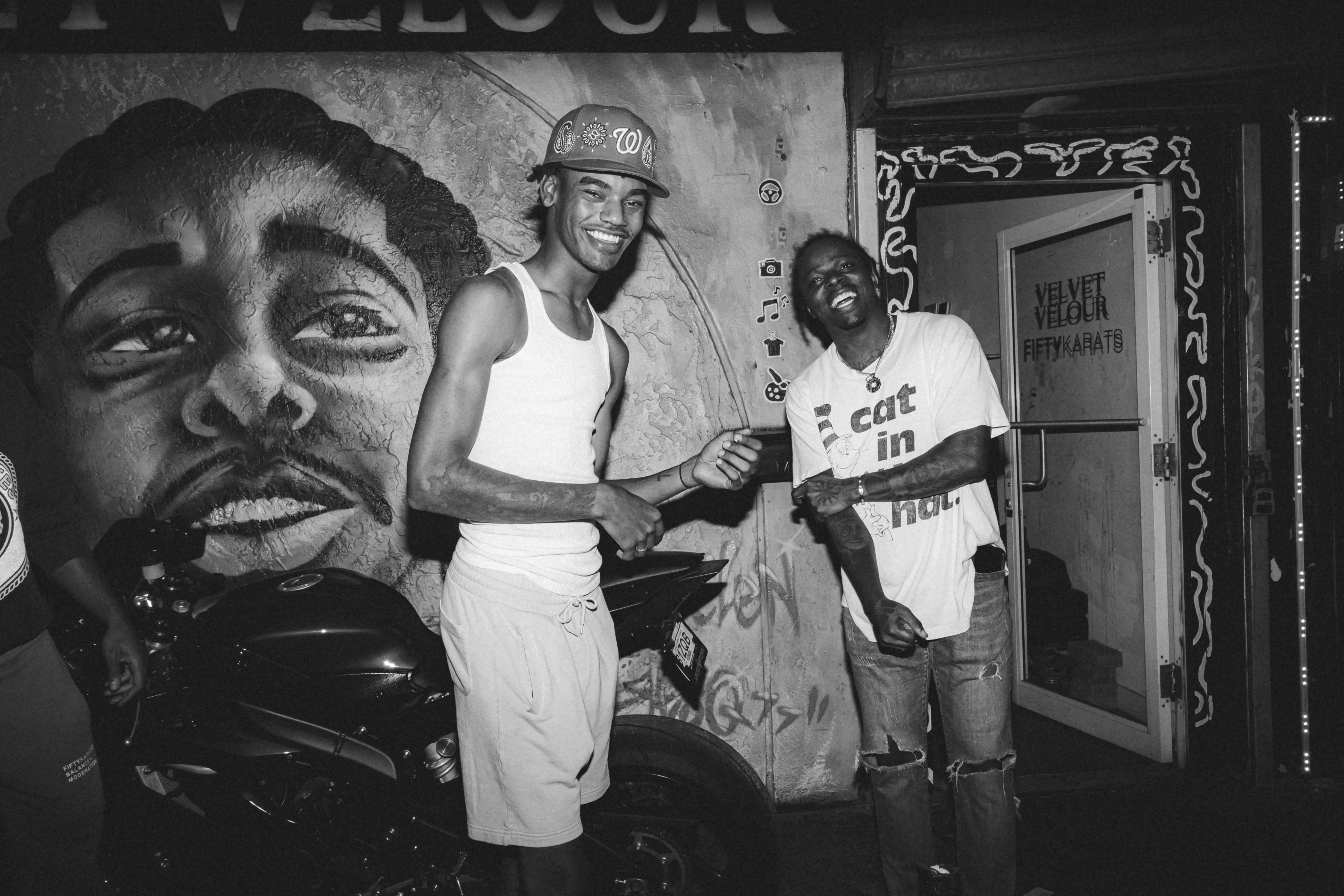 Two men stand in front of a mural that was created while listening to classic retro hip hop songs