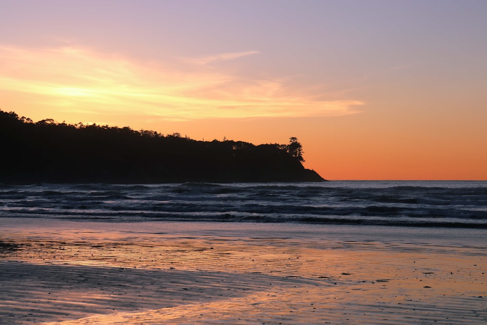 the sun is setting over the ocean with a small island in the distance