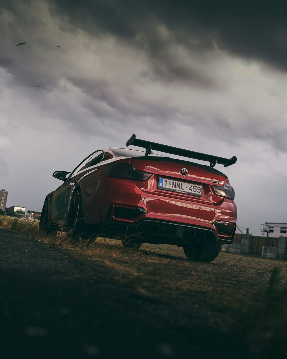 a red car parked on the side of a road under a cloudy sky