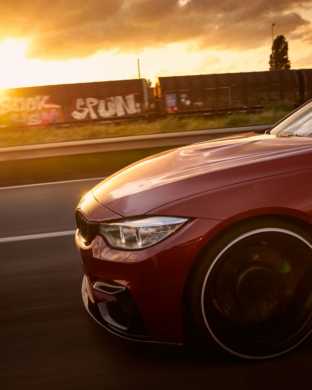 a red car driving down the road at sunset