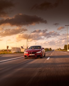 A vibrant red muscle car with bold stripes cruising down an open highway at sunset.