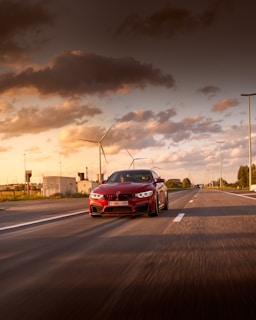 A vibrant red muscle car with bold stripes cruising down an open highway at sunset.