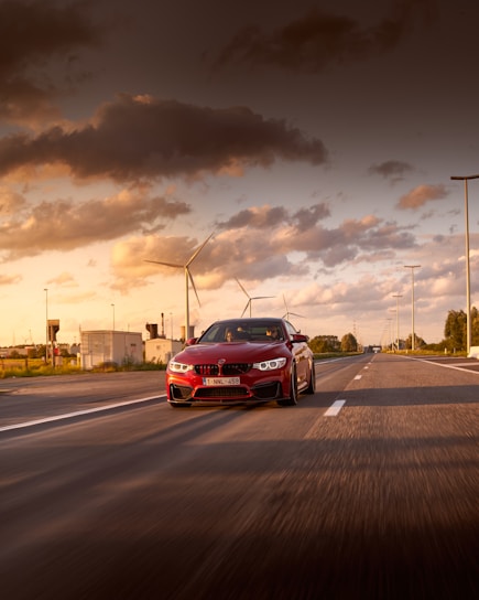 A sleek red hot rod speeding down an open highway at sunset