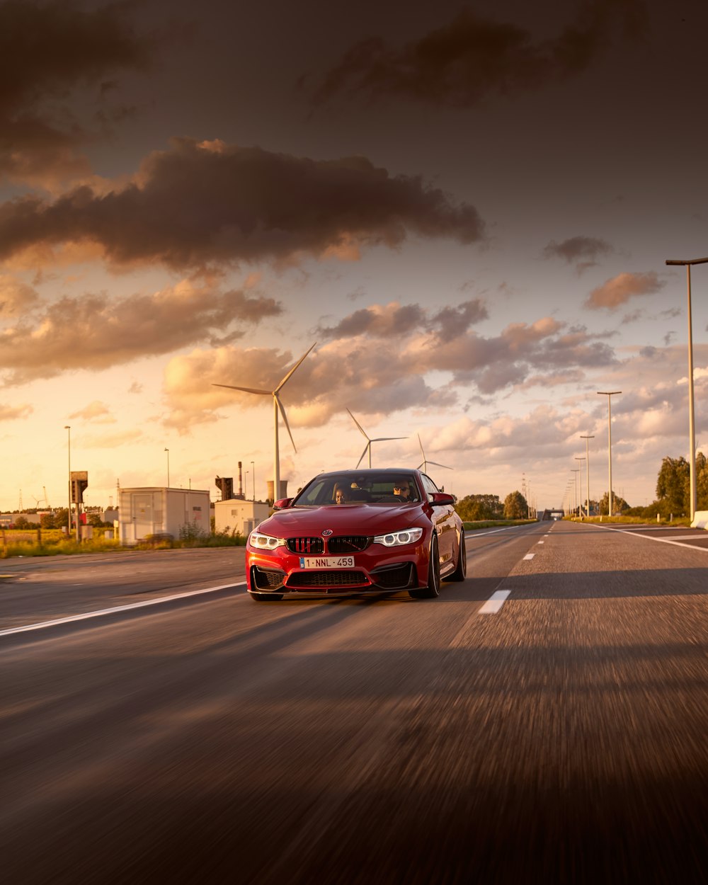 a red car driving down a street next to wind mills