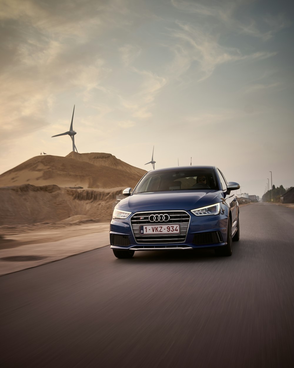 a blue car driving down a road with windmills in the background