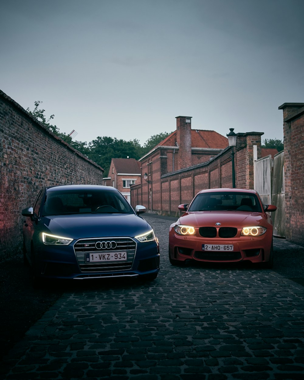 two cars parked next to each other on a cobblestone road