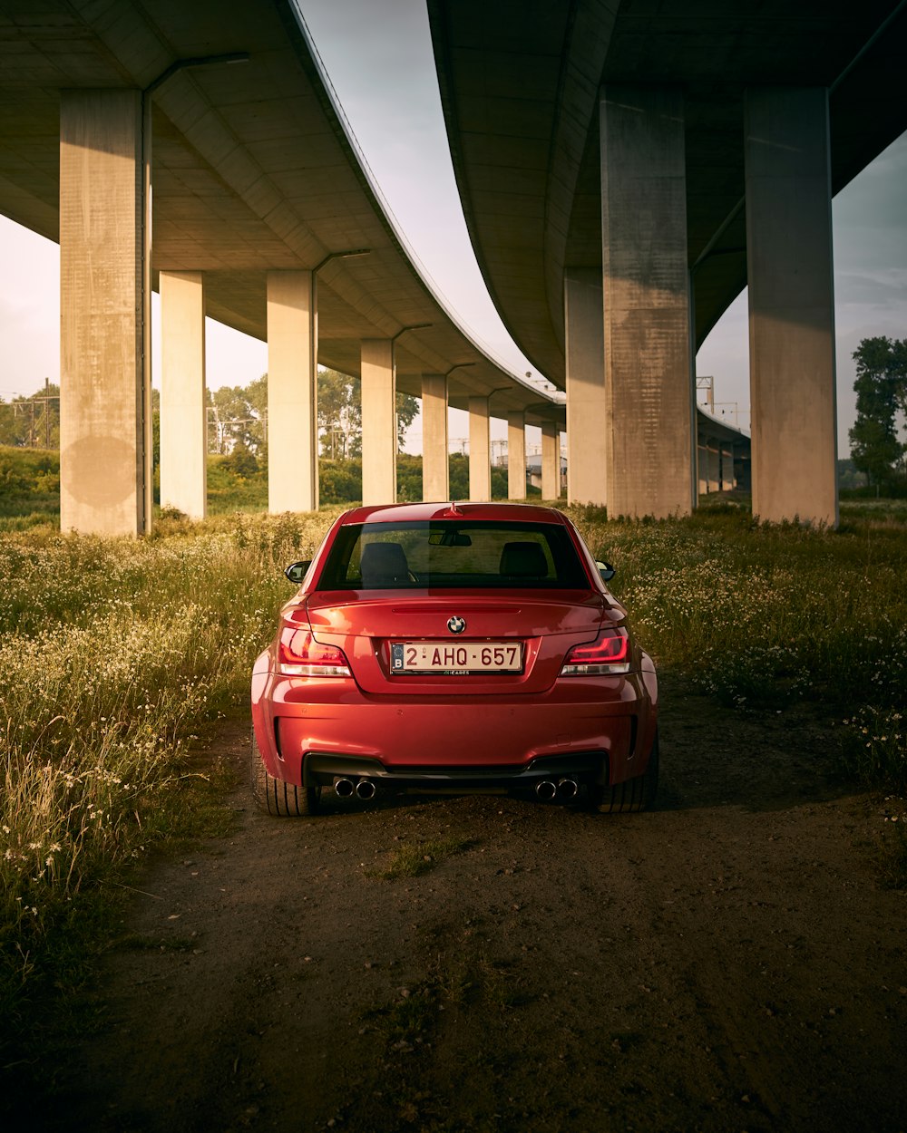 a red car parked in front of a highway under a bridge