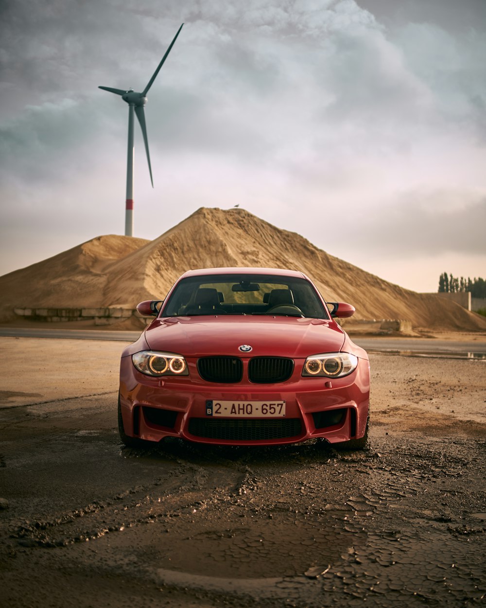 a red car parked in front of a wind turbine