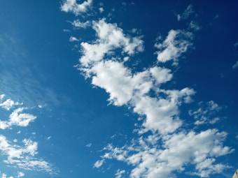 The image features a clear blue sky scattered with fluffy white clouds. The clouds are spread unevenly and have a soft, wispy appearance. The overall composition conveys a sense of openness and tranquility.