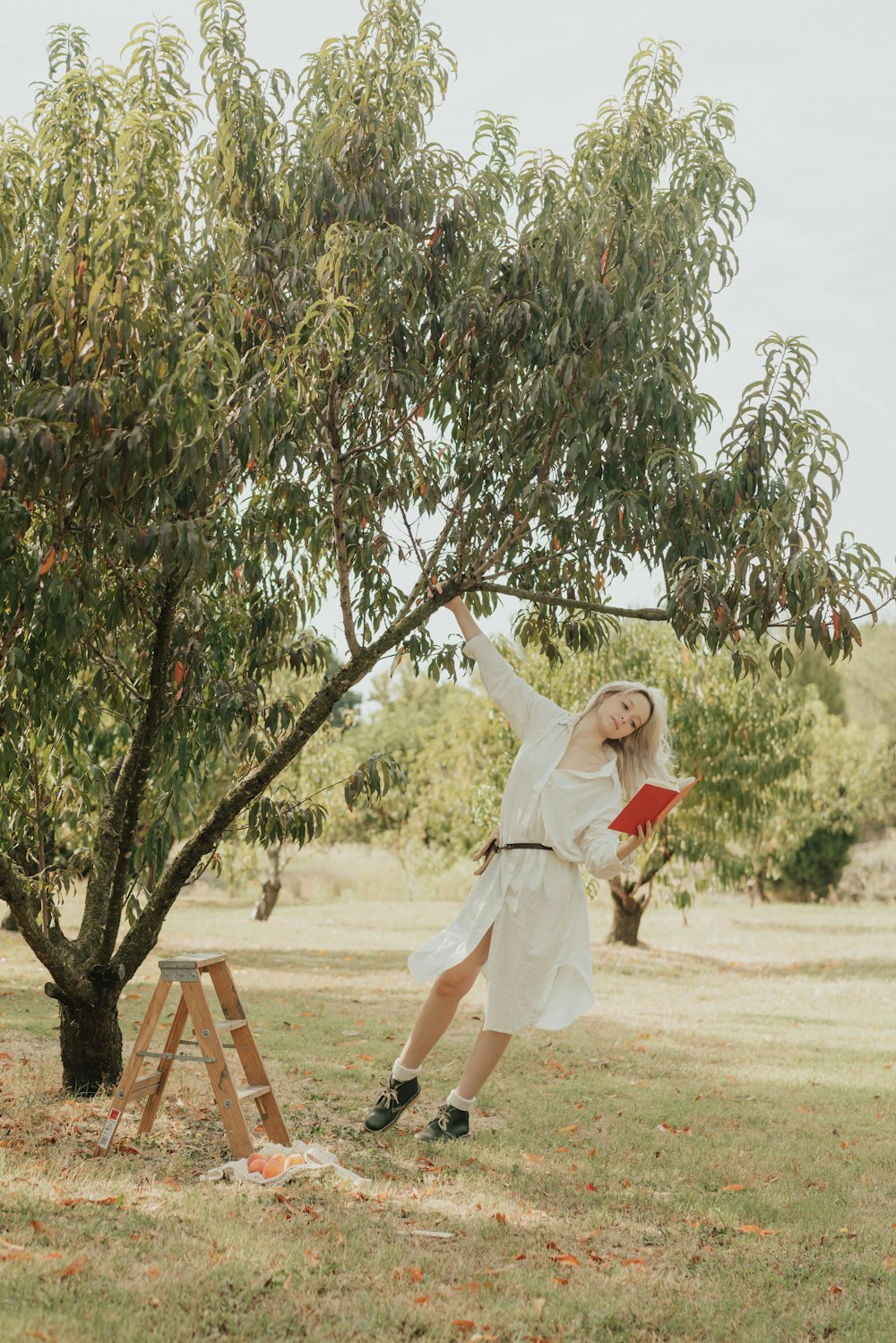 a woman in a white dress reaching up to a tree