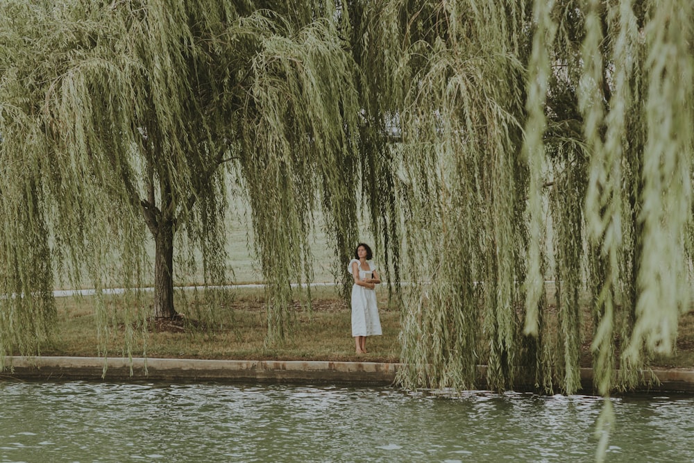 a woman standing in front of a tree next to a body of water