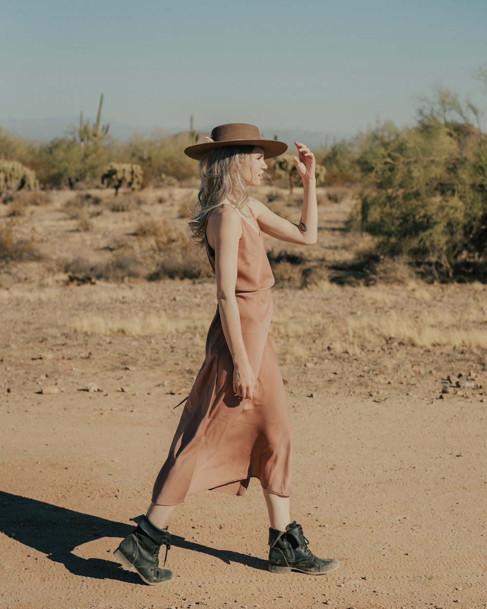 a woman walking across a dirt field wearing a hat