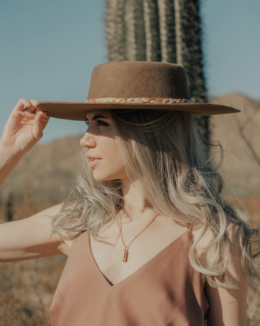 a woman wearing a hat standing in front of a cactus