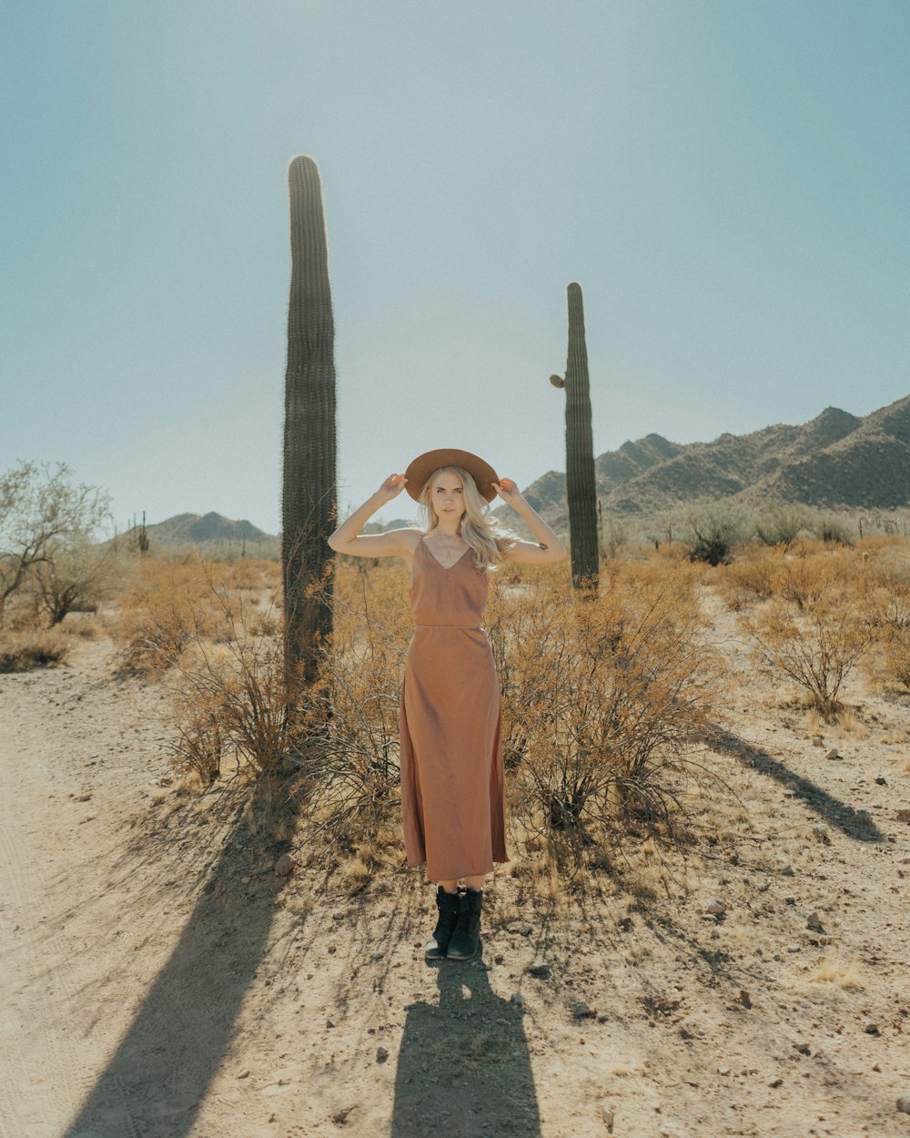 a woman wearing a hat standing in front of a cactus