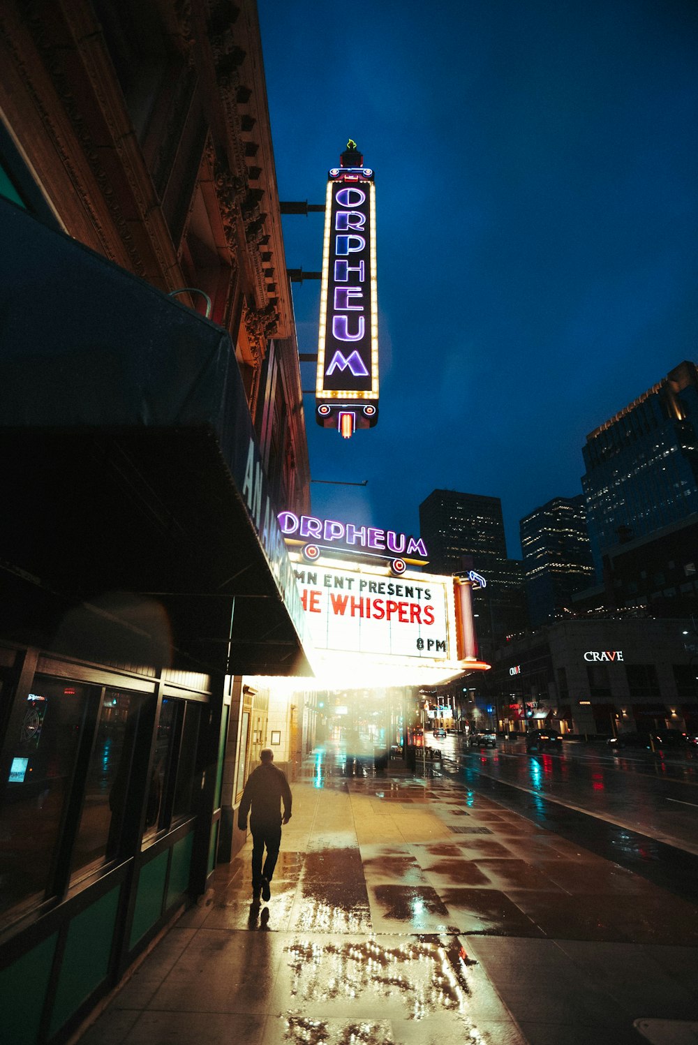 a man walking down a sidewalk in front of a theater