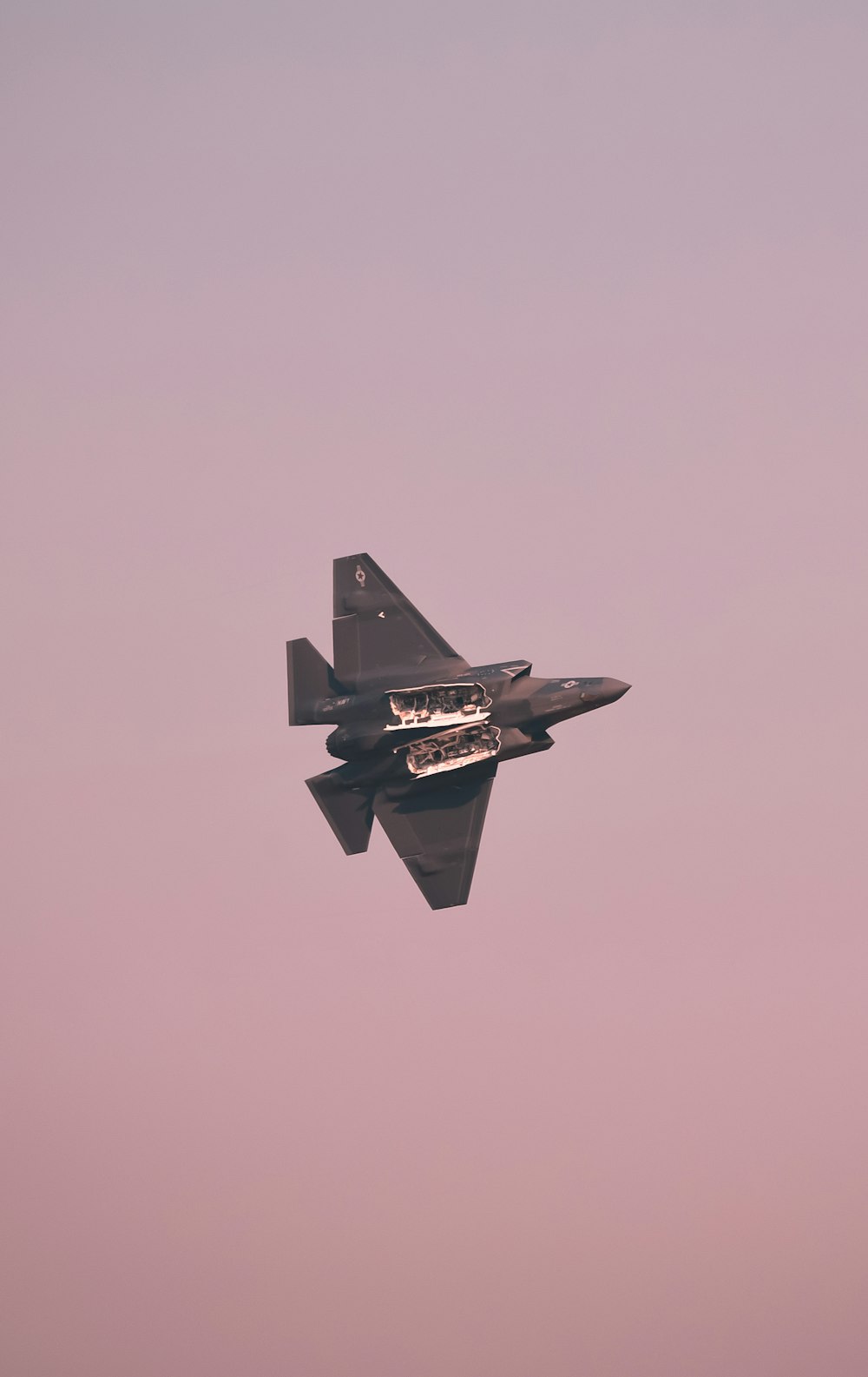 a fighter jet flying through a pink sky