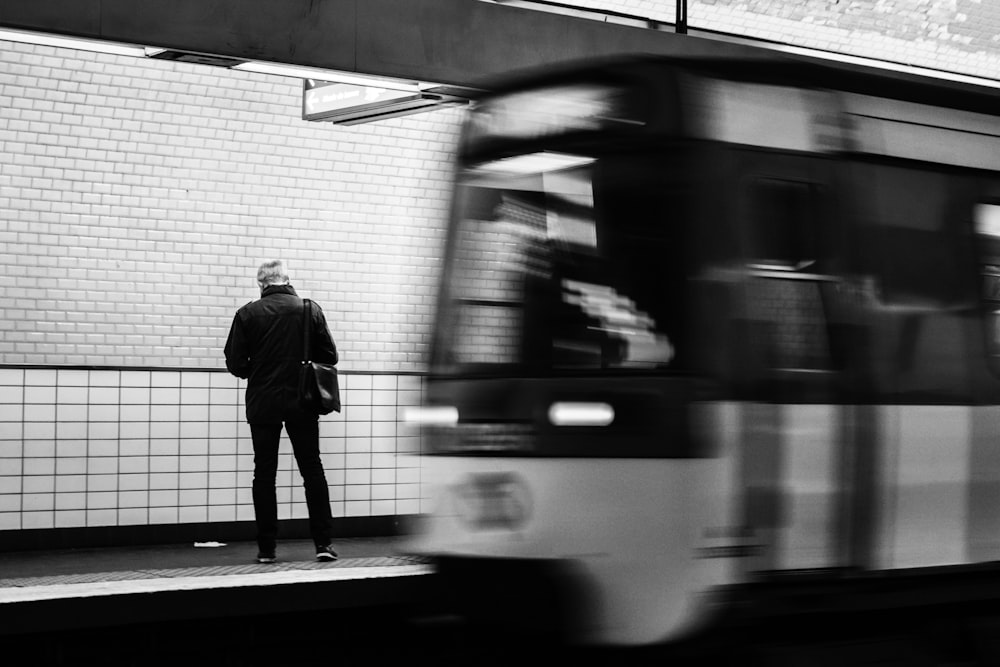 a black and white photo of a man waiting for a train